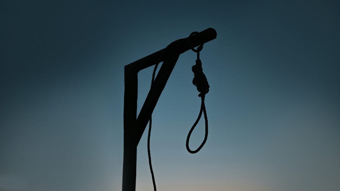 A rope tied to a wooden post in front of a building, resembling a gallows