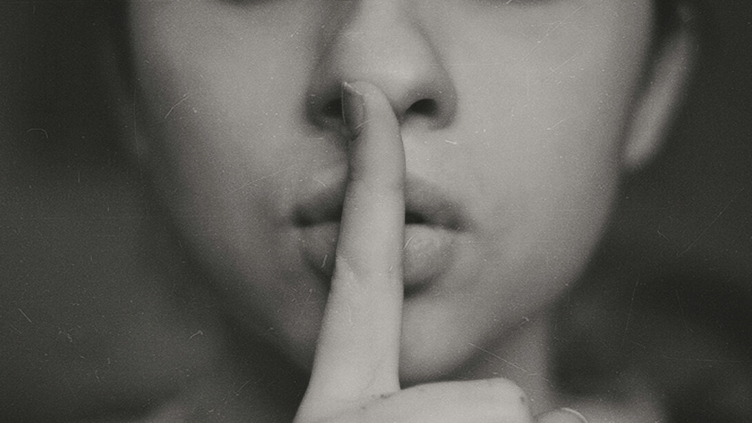 Close up of a woman's index finger pressed against her mouth, calling for quietness