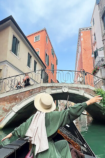 During her expat journey, a woman finds herself in a gondola, absorbing the enchanting charm of Venice, Italy, while gliding through its picturesque waterways