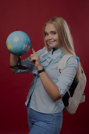 Blonde student holding a globe and indicating a spot, symbolizing the excitement of being an international student, engaging in cultural exchange, and embarking on travel adventures