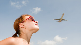 A young woman gazes at an airplane crossing the sky, imagining a new life beyond the horizon