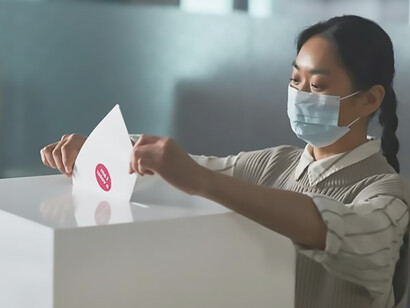 A woman votes and puts the envelope into the box