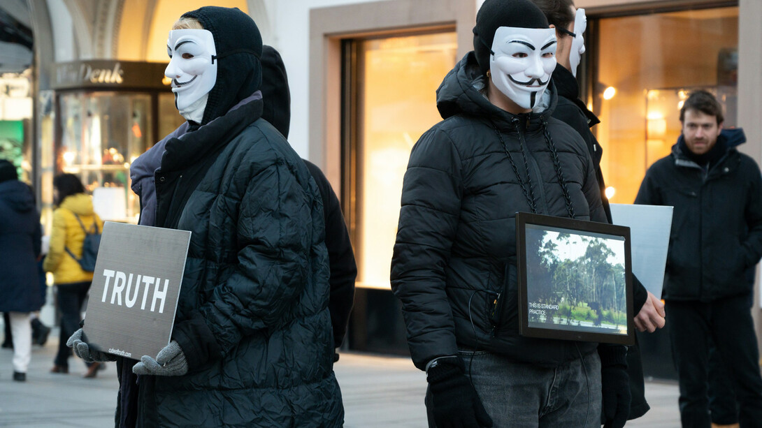 Masked figures holding placards to demand the truth
