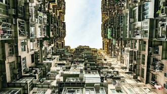 Low-angle view of a towering residential building in Hong Kong, reflecting the stark contrast between urban density, inequality, and poverty