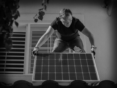The man lifts the solar panel in place while standing on the roof
