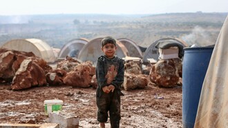 A young boy stands in the mud at a refugee campsite