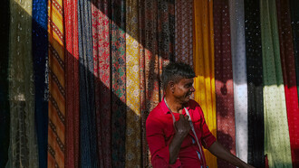 Man measuring fabrics at a market stall in India, selling textiles with care and precision
