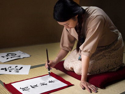 A woman practicing Japanese calligraphy, carefully writing kanji characters that embody the Japanese philosophy of Oubaitori
