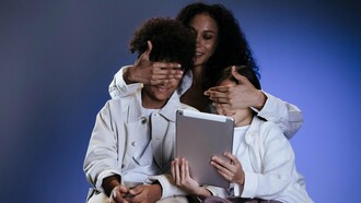 Uma mãe cobre os olhos dos filhos enquanto eles seguram um tablet diante da tela. Em tempos de hiperexposição digital, proteger também significa compreender o que os adolescentes consomem online. O gesto de proteção contrasta com a presença constante das telas no cotidiano infantil. A supervisão digital tornou-se parte essencial do cuidado emocional e cognitivo. Entre curiosidade e vulnerabilidade, crianças e adolescentes acessam conteúdos para os quais muitas vezes ainda não possuem maturidade emocional. O cérebro em formação responde intensamente aos estímulos digitais