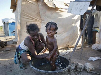 Madre haitiana bañando a su hijo en un campamento