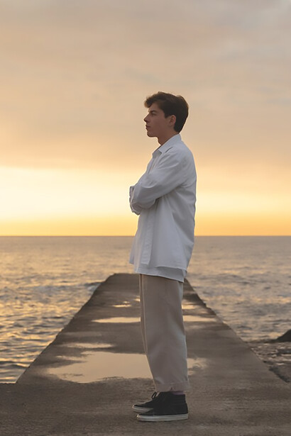 At the seashore during sunset, a man stands immersed in contemplation, as if drowned in his own thoughts