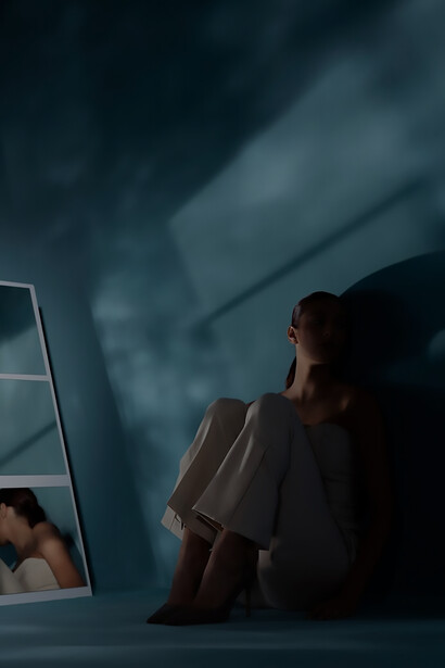 In a striking image, a woman seated on the floor wears heels, her reflection elegantly captured in the adjacent mirror