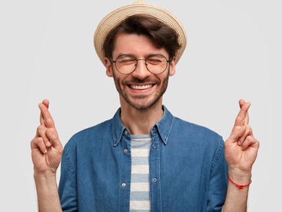The poignant moment of a brunet man, adorned in a denim shirt and hat, crossing his fingers as he releases expectations and surrenders to the flow of life, depicted in this compelling image