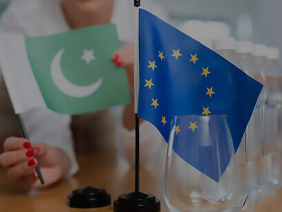 A woman secretary arranges an office for negotiations, placing flags of the European Union and Pakistan on the table, symbolizing diplomatic engagement and international dialogue