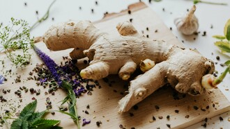 A piece of ginger on a cutting board with some aromatics, representing the importance of the fresh ingredients that add depth and complexity to dishes