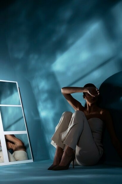 A woman sits on the floor with a contemplative expression, surrounded by soft natural light, her posture exuding introspection and serenity