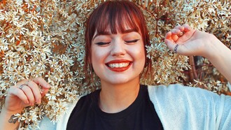 A woman in a black crew-neck top and white cardigan lies among the daisies