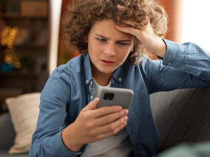A young man looking at his phone with an upset expression, highlighting the stress caused by consuming negative news