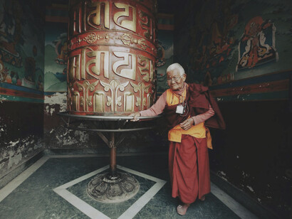 Elderly monk walking around prayer wheel