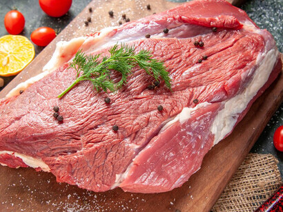 Fresh, raw red meat on a wooden cutting board, accompanied by a nude-colored towel, lemon, and garlic, set against a multicolored background