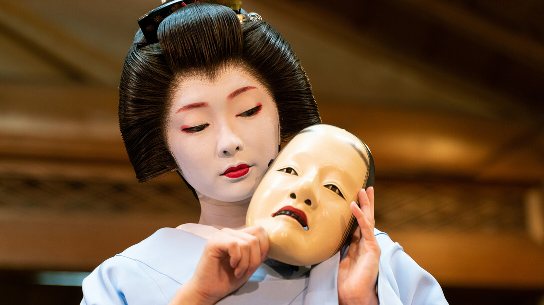 Kyoto geiko Toshimana, adorned in full makeup and a katsura wig, elegantly holds a Nō mask on the picturesque Kawamura Noh Stage, Japan
