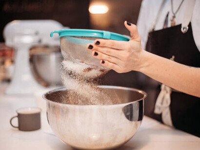 A hand gently sifts flour using a sieve, demonstrating the process of filtration