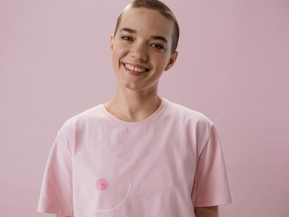 A smiling woman in a pink shirt, with symbol signaling breast cancer survivr