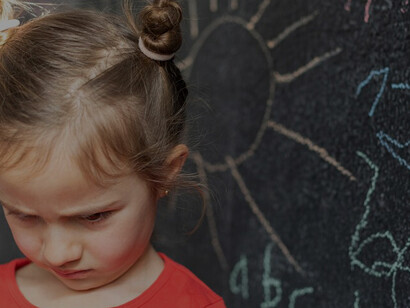 A distressed young girl displays signs of dysregulation while standing in front of a blackboard in a classroom environment