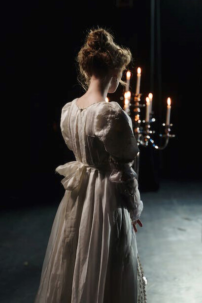The back view of a woman gracefully holding a candelabrum on a theater stage