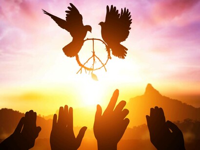 Two doves holding the symbol for peace, flying over the sunset, with hands stretched to touch them