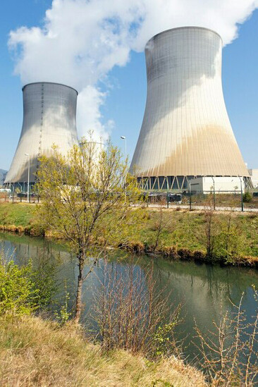 In the warmth of summer, smokestacks rise above a nuclear facility, framed by the calm waters of a nearby river