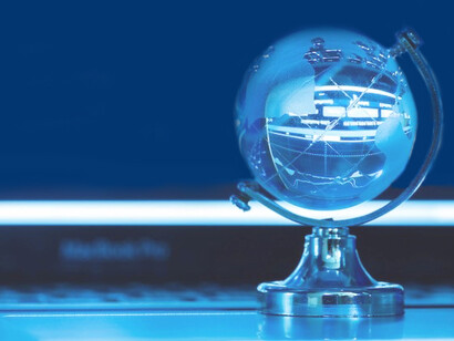 A crystal globe set against a computer screen with stock market graphs, representing the interconnectedness of global economies