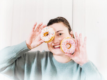 A heavier woman holds up two donuts which are a common breakfast food in developed countries