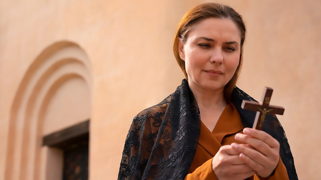 A woman prays with a crucifix in her hands before the cathedral
