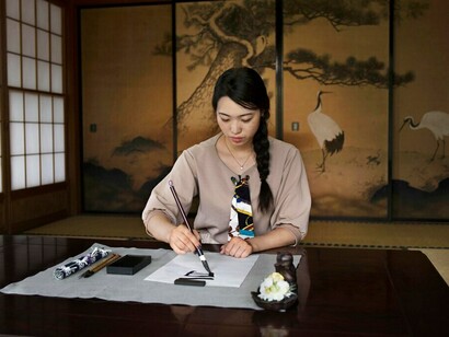 Immersed in Japanese calligraphy, a woman writes kanji symbols that capture the essence of Oubaitori, a philosophy celebrating unique personal growth and individuality