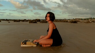 Uma mulher contempla o horizonte diante da máquina de escrever, como quem se prepara para transformar silêncio em narrativa. Entre a vastidão do mundo e a intimidade das palavras, nasce o poder sedutor da escrita
