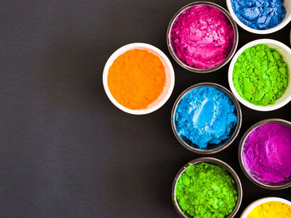 An overhead view of bowls filled with vibrant Holi powder against a black backdrop offers a striking representation of color psychology, including emotional responses