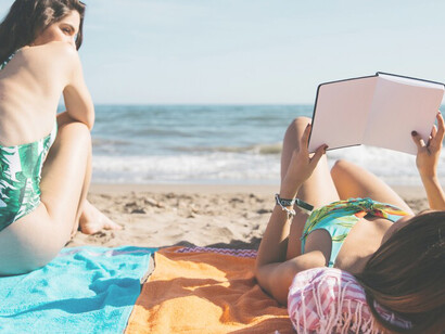 A woman and her friend enjoying a digital detox holiday at the beach, immersed in nature and travel while reading a book
