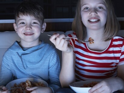 Dos niños cenando delante de la televisión