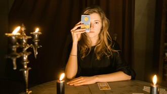 Uma mulher observa atentamente cartas dispostas sobre a mesa durante uma leitura de tarot. Entre símbolos e interpretações, o artigo convida a refletir sobre como práticas voltadas ao autoconhecimento podem ampliar a compreensão de si, mas também reforçar crenças limitantes quando passam a orientar decisões de forma acrítica