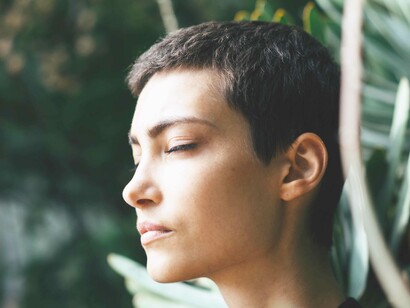 A woman with eyes closed concentrating deeply in her meditation in her zen garden
