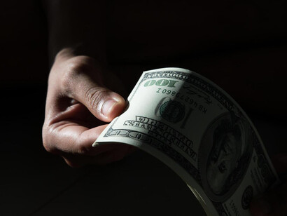 A person holds a handful of dollar bills, the currency visible between their fingers