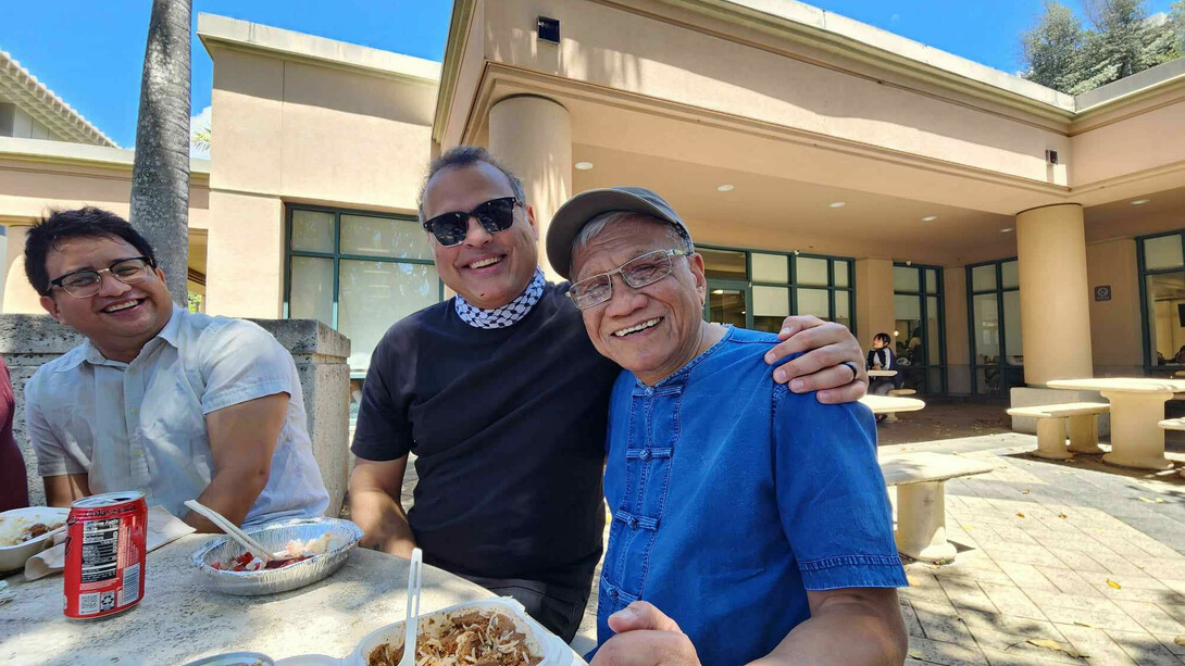 Vijay Prashad, Walden Bello and another participant smile while sharing a meal on a courtyard