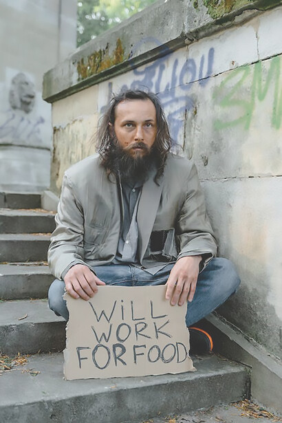 A man, clutching a cardboard sign that reads 'Hungry and in need of help for food,' stands as a poignant symbol of unmet needs in the face of adversity