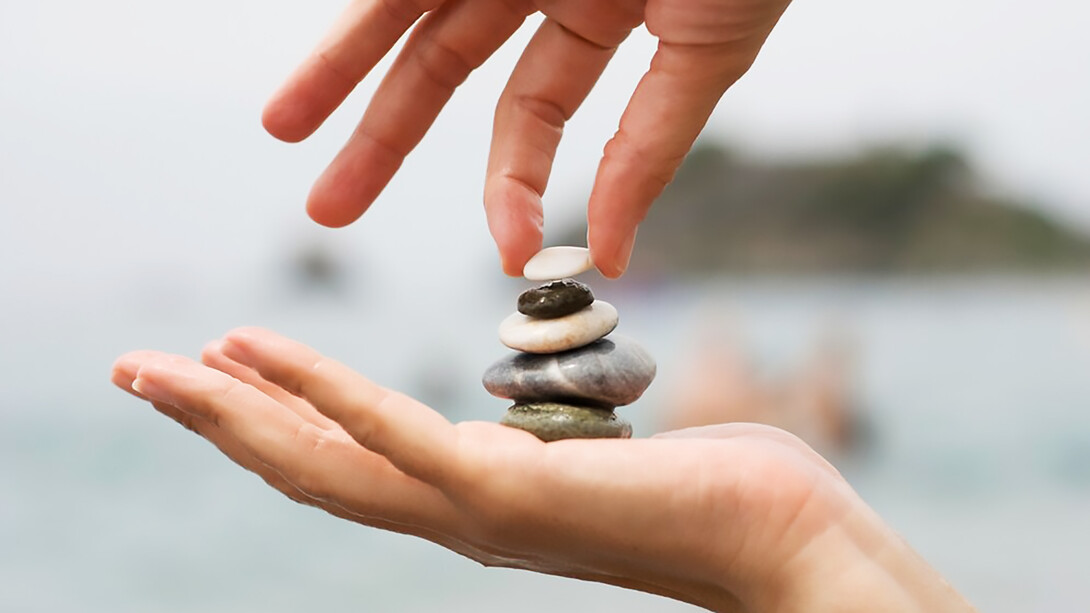 A woman's hands delicately place the final pebble atop a stack of stones, symbolizing completion and mindfulness