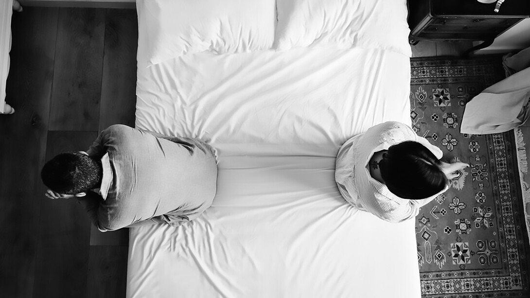 A couple sits on the bed, separated by their fear of intimacy