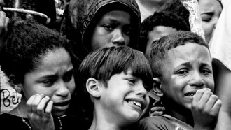 Crianças durante o velório e enterro de seu amigo, Thiago Menezes Flausino, de 13 anos, morto pela polícia. O registro foi feito pela fotógrafa Selma Souza em 2023, no Rio de Janeiro, Brasil. A pessoa deixa de ser João, Mariah, Benhur e passa a ser o maconheiro, o ladrão. Esse caso escancara a aceitação da violência policial contra adolescentes pobres e a necropolítica que decide que a vida de Benhur não importa