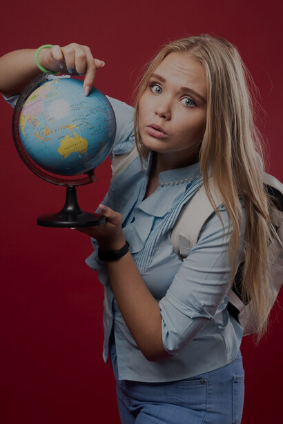 Blonde female student with a globe, pointing to a destination, representing international student experiences, cultural exchange, travel adventure, and exploring new cultures