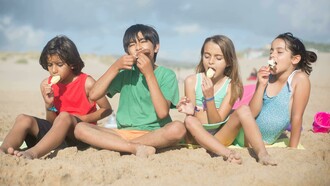 Children sitting on the sand in Portugal, enjoying ice cream sticks