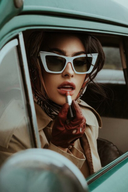 A woman sitting in the back seat of a vintage car, wearing sunglasses and a scarf, evoking a sense of nostalgia